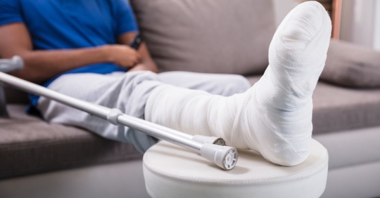 Hombre con pierna lesionada apoyado en su casa